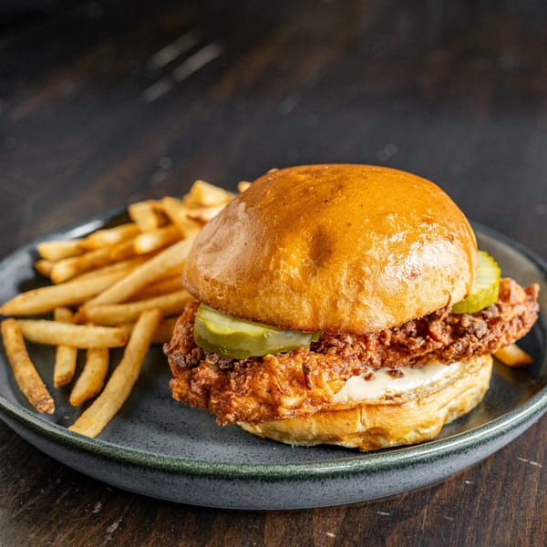 Crispy fried chicken sandwich with pickles and mayonnaise on a bun, served with french fries.