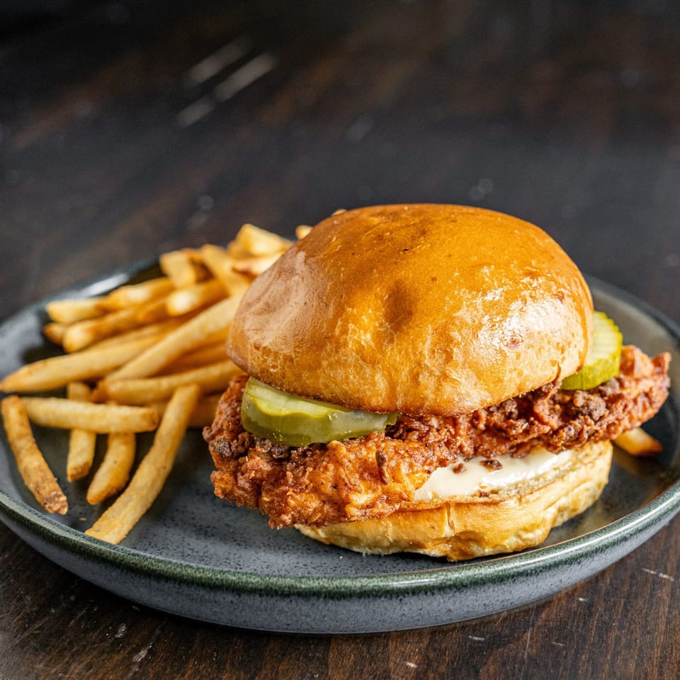 Crispy fried chicken sandwich with pickles and mayonnaise on a bun, served with french fries.