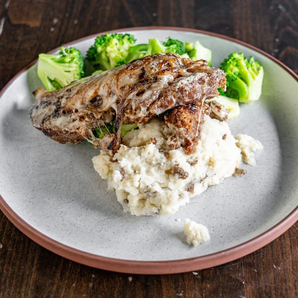 Melted cheese burger patty over mashed potatoes with broccoli on a gray plate.