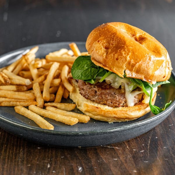 A Steam Pub burger with melted cheese, spinach, and caramelized onions, served with golden fries.