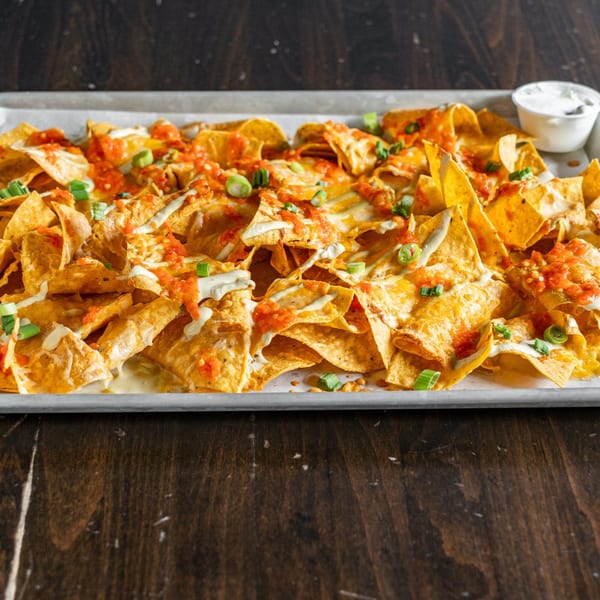 A large tray of Steam Pub nachos with melted cheese, salsa, green onions, and a side of sour cream.