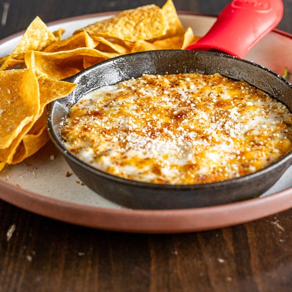 Skillet of melted cheese dip with spices, served with tortilla chips on a rustic plate.