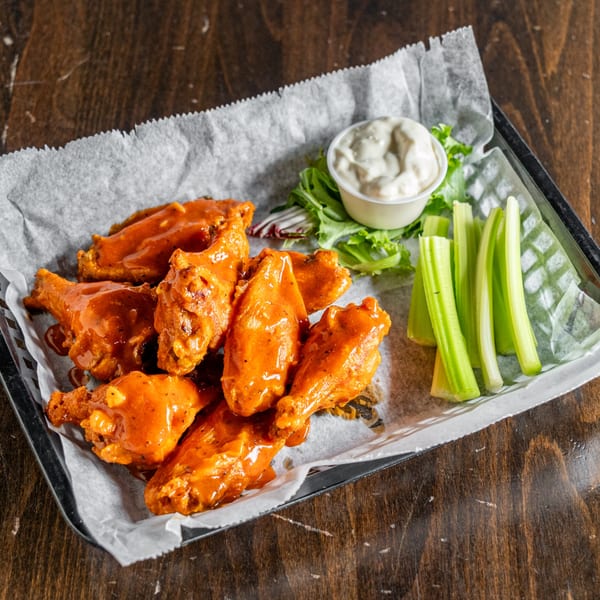 A tray of buffalo wings with celery sticks, lettuce, and a side of ranch dressing.