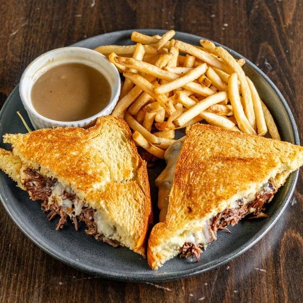 A grilled cheese sandwich with pulled pork, fries, and a side of gravy on a dark plate.
