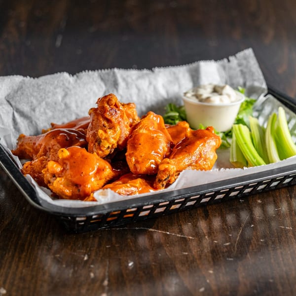 Buffalo wings in a basket with celery sticks and a side of blue cheese dressing.
