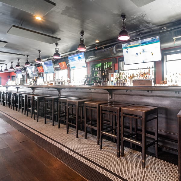 Long wooden bar with stools, multiple TVs showing sports, and a well-stocked liquor shelf at Steam Pub.