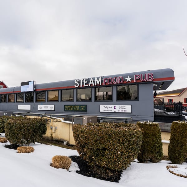 Exterior of Steam Pub, a gray building resembling a train car, with snow-covered bushes in the foreground.
