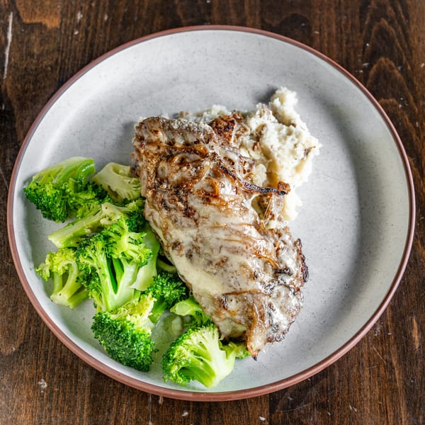 A plate of meatloaf with gravy, mashed potatoes, and steamed broccoli on a wooden table.